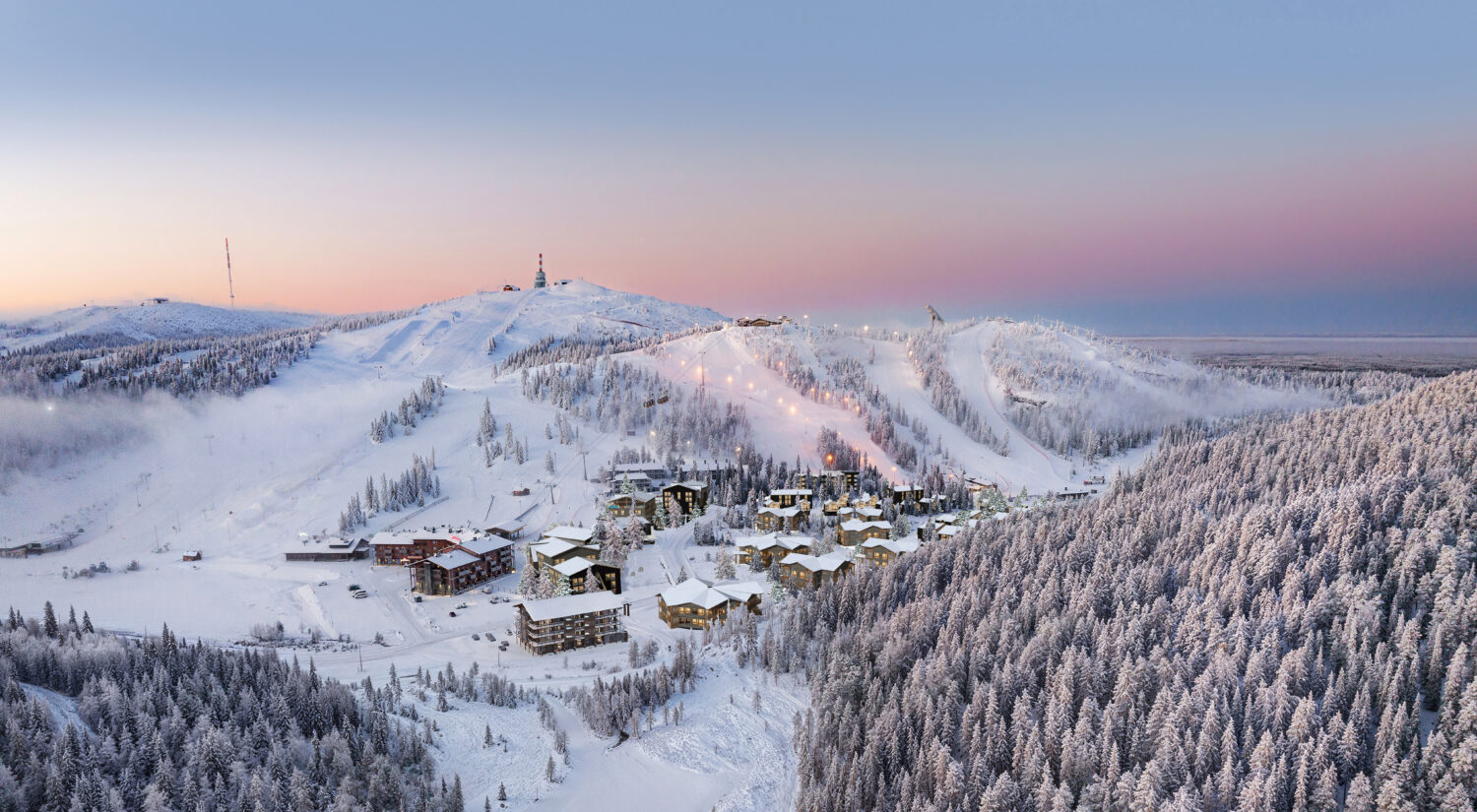 Panoramic winter view of Ruka ski resort in Kuusamo, Finland with snowy slopes, forest and village at dusk