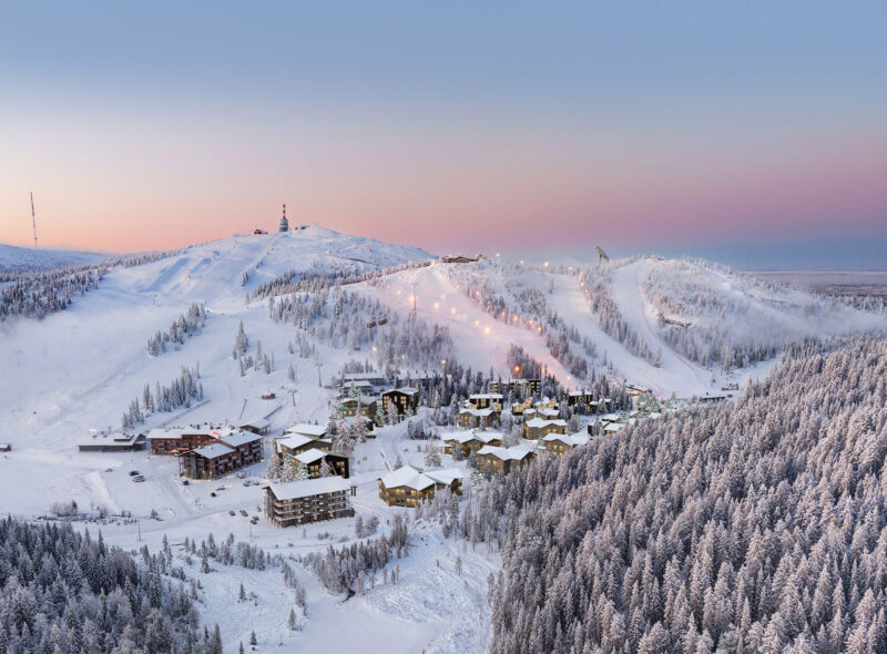 Panoramic winter view of Ruka ski resort in Kuusamo, Finland with snowy slopes, forest and village at dusk