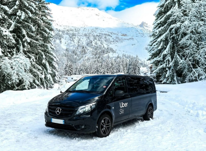 Uber Ski van parked on a snowy mountain road, surrounded by snow-covered pine trees.