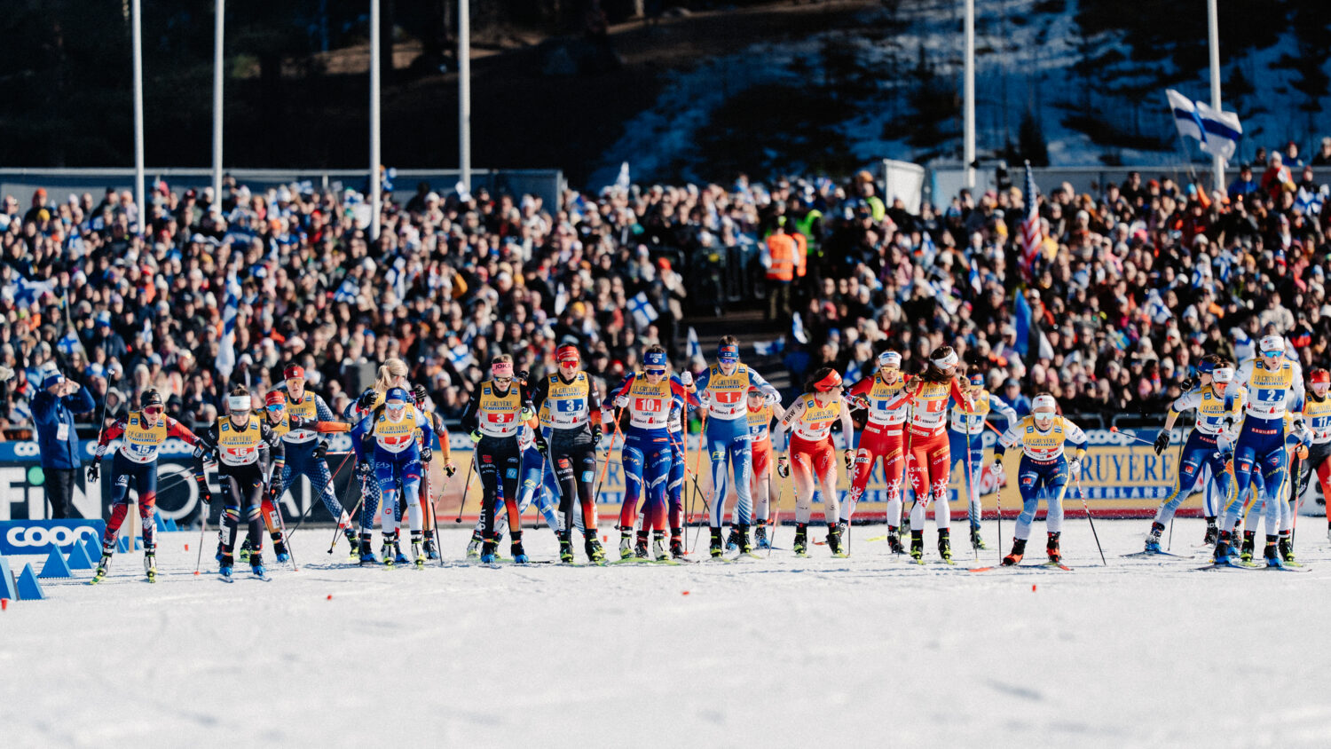 Cross-country skiers start a team sprint race at the Lahti Ski Games in front of a large crowd.